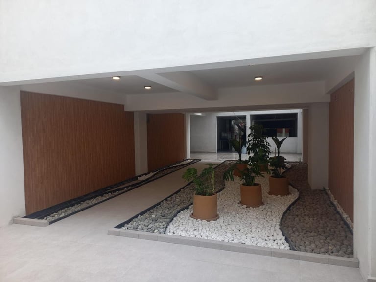 Modern carport and entrance with wooden walls, potted plants on gravel, and concrete flooring in minimalist design